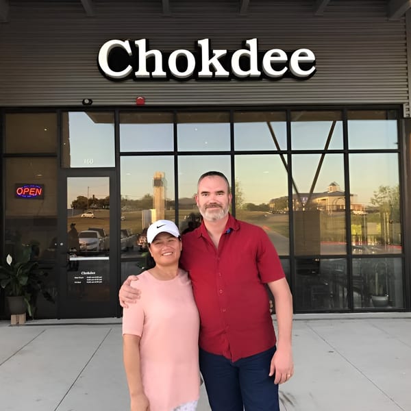 A man and woman stand smiling in front of the Chokdee restaurant entrance.