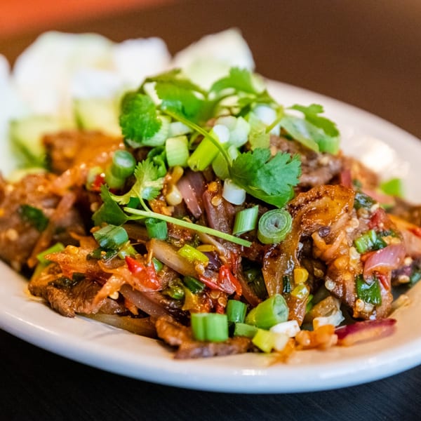 Spicy Thai beef salad with red onions, chili, and fresh herbs on a white plate.