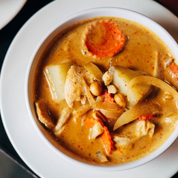 Close-up of a bowl of yellow curry with chicken, potatoes, carrots, onions, and peanuts.
