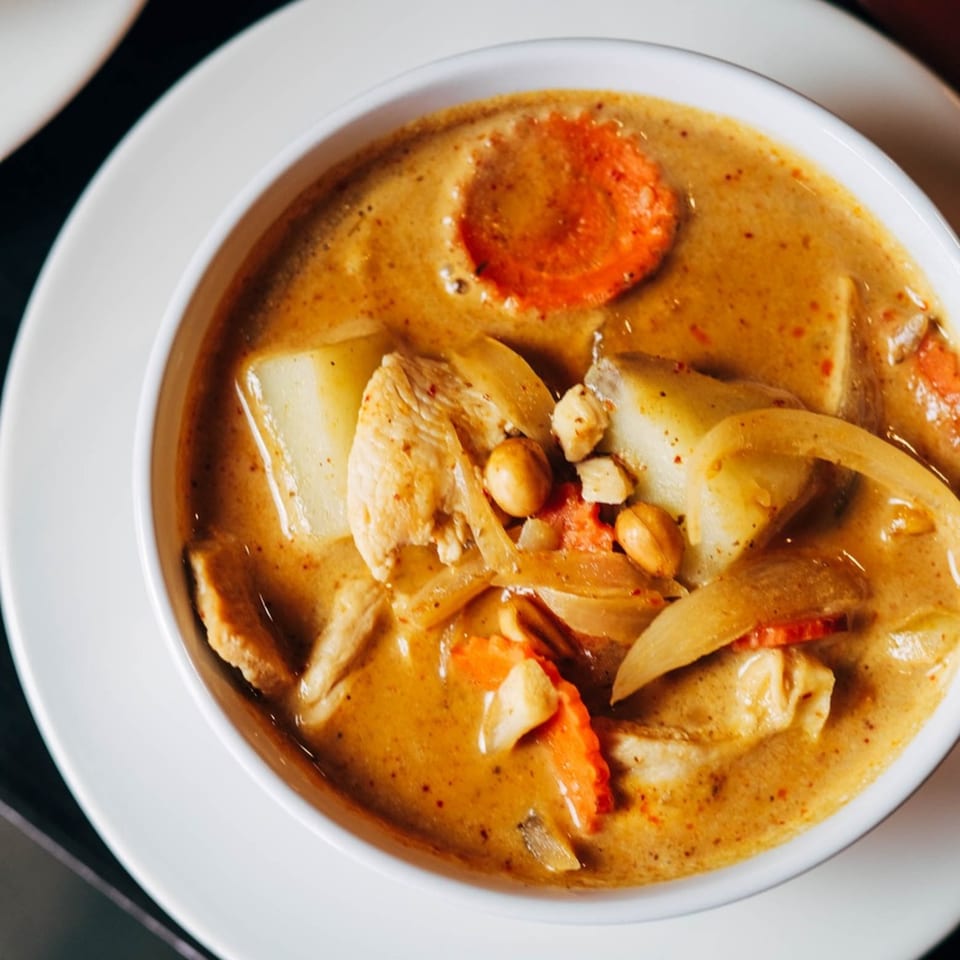 Close-up of a bowl of yellow curry with chicken, potatoes, carrots, onions, and peanuts.