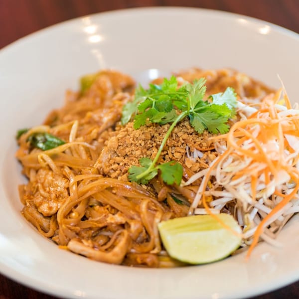 Pad Thai noodles with crushed peanuts, cilantro, bean sprouts, shredded carrots, and a lime wedge.
