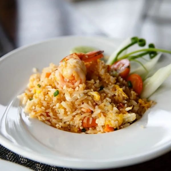 Shrimp fried rice with vegetables, cherry tomatoes, and lime on a white plate.