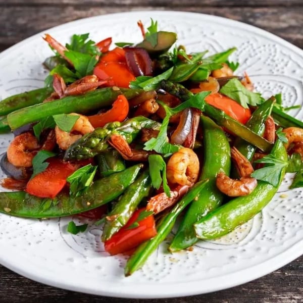 A vibrant stir-fry of shrimp, red bell peppers, and green snap peas on a white plate.